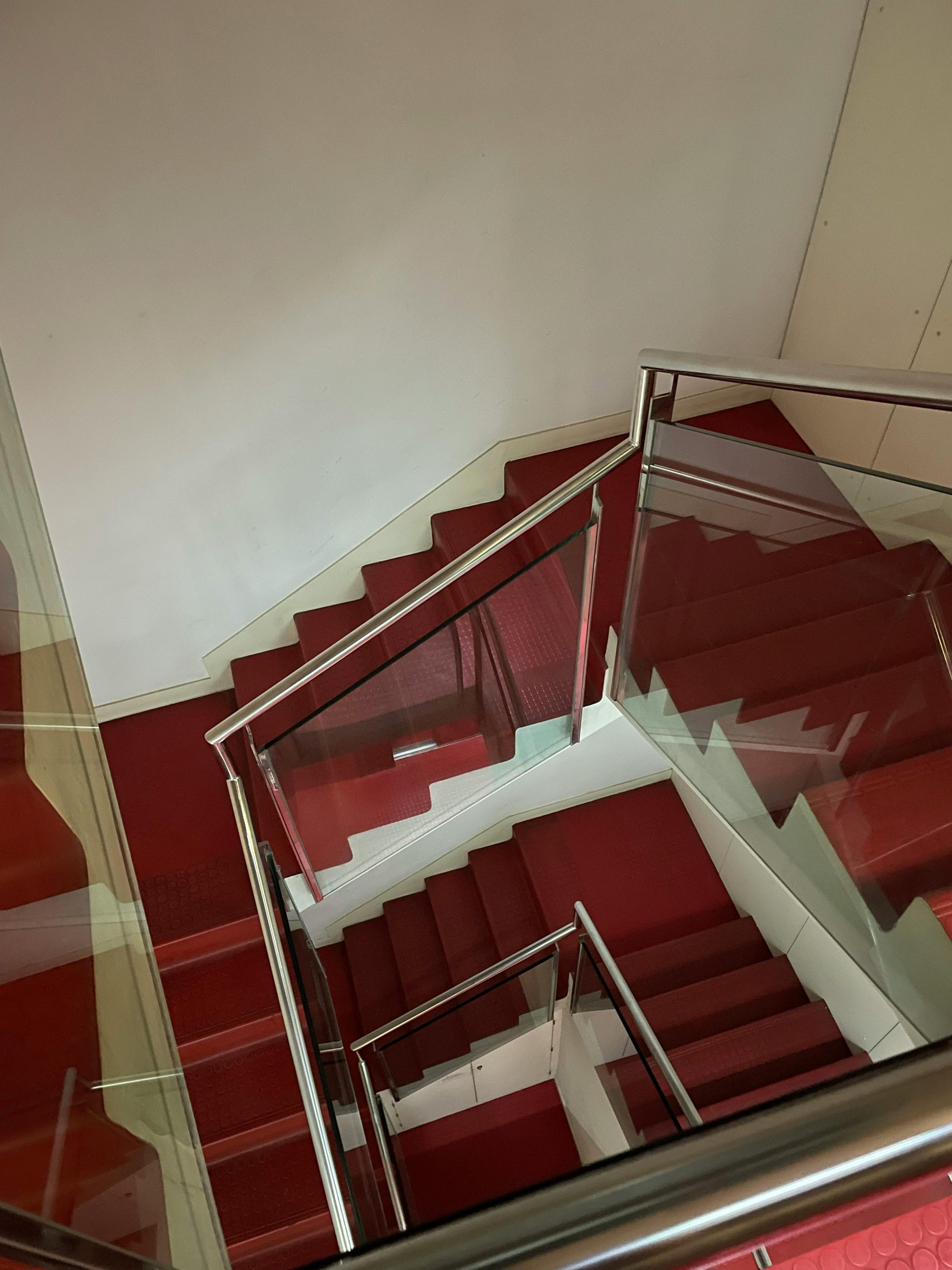 Vue en plongée d'un escalier moderne recouvert de moquette rouge, de rampes métalliques élégantes et de murs blancs.